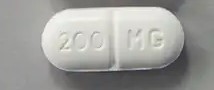 A close-up shot of a white, capsule-shaped 200 mg modafinil pill with a center score line.