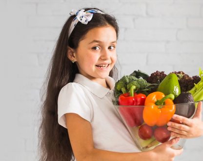 Smiling kid carrying a lot of fruits and vegetables good for oral health.
